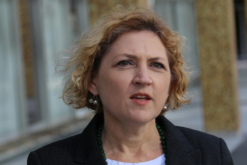 A woman with curly blonde hair stands outside the ACT Assembly.