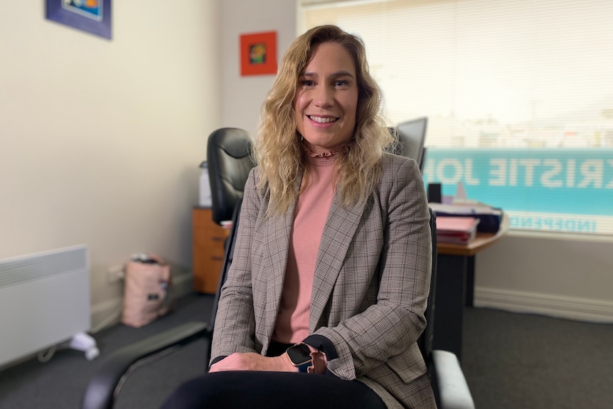 A woman sits in an office smiling at the camera.