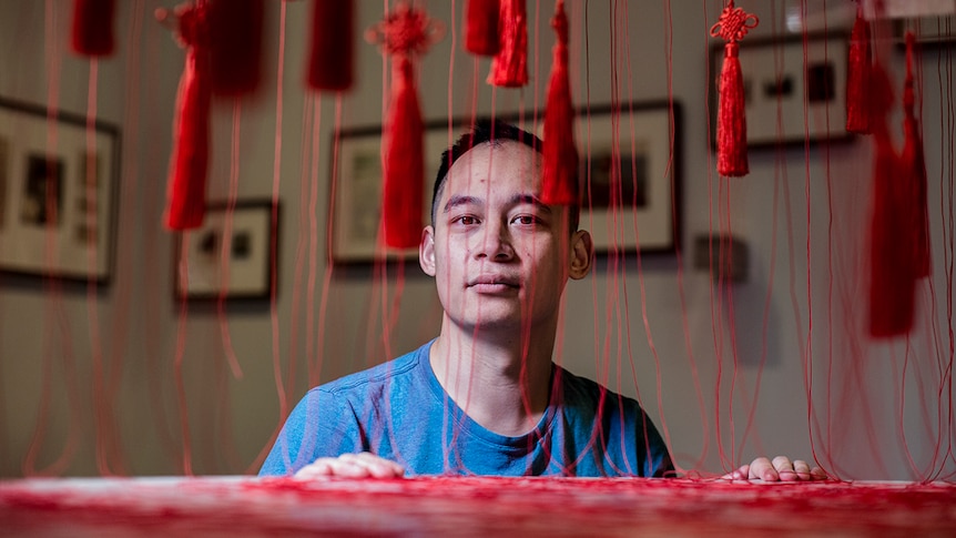 Colour photo of Phuong Ngo posing with his installation artwork titled Colony at the Museum of Contemporary Art in Sydney.