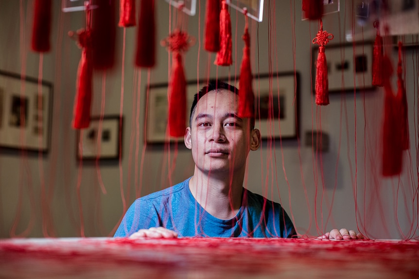 Colour photo of Phuong Ngo posing with his installation artwork titled Colony at the Museum of Contemporary Art in Sydney.