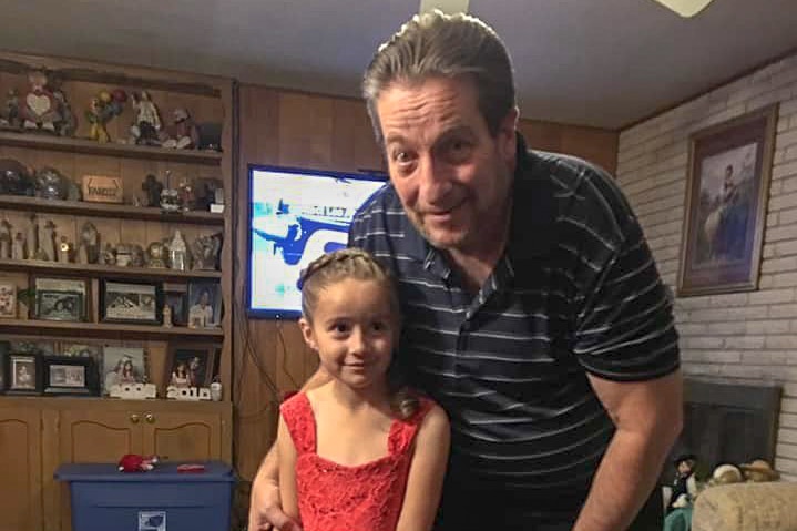 An older man puts his arm around a little girl in a red dress