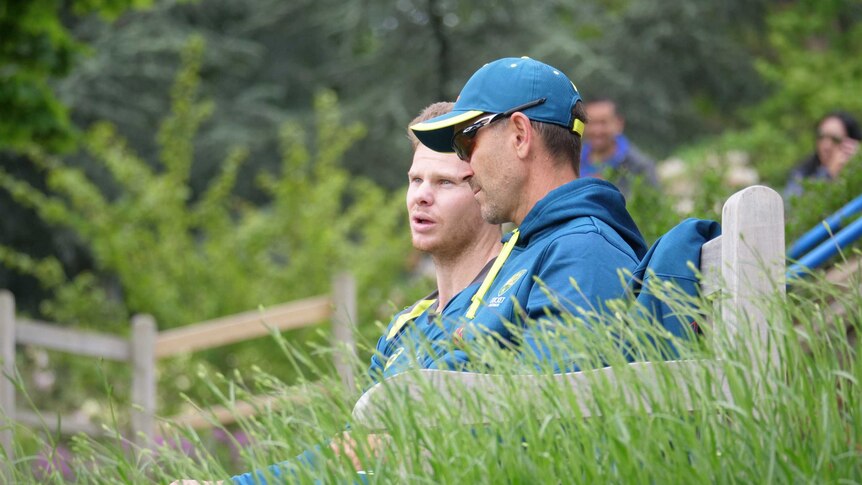Justin Langer and Steve Smith sitting on a park bench having a private conversation.