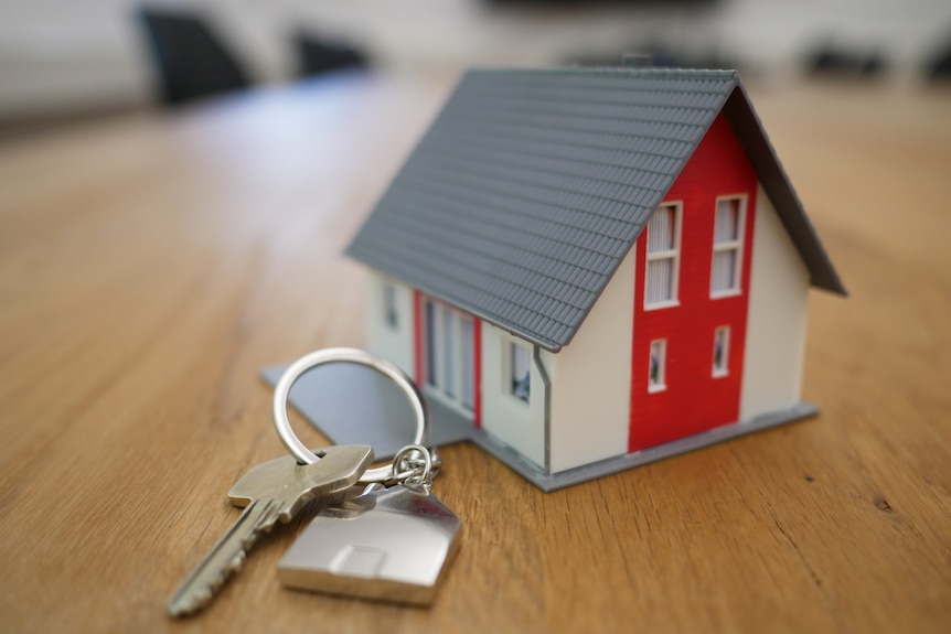 A mini house keyring and a set of keys on a wooden table 
