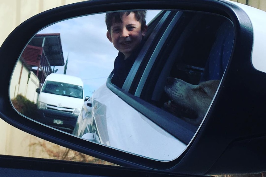 A boy smiles in a car rear vision mirror