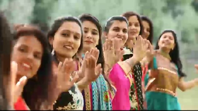Women stand in a line in colourful costumes dancing in Bollywood style.