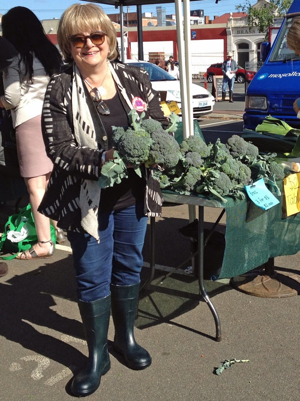 Jane Adams holds a bunch of organic broccoli wearing Wellington boots
