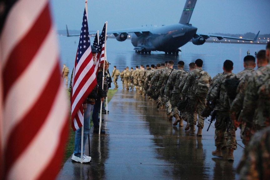 A line of US army troops walk towards a large aircraft