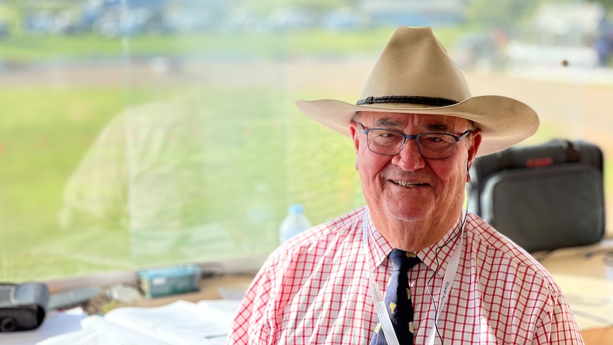 Man with glasses in a broad-brimmed hat and checked shirt smiling at camera.