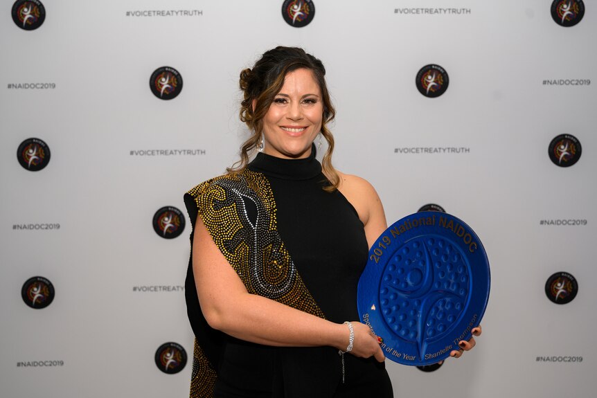  Shantelle Thompson poses for a portrait at the 2019 National NAIDOC Awards with a large blue shield.