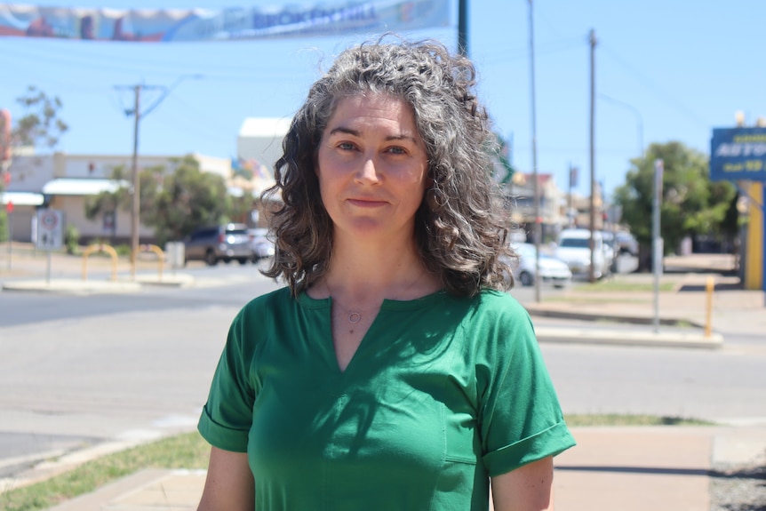 A woman in a green dress smilling standing in front of a streetscape