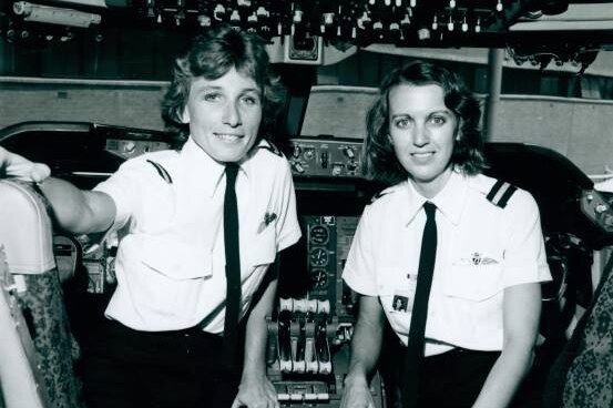 Sharelle Quinn and Ann Bennett stand inside the cockpit of a plane wearing their pilot's uniform.