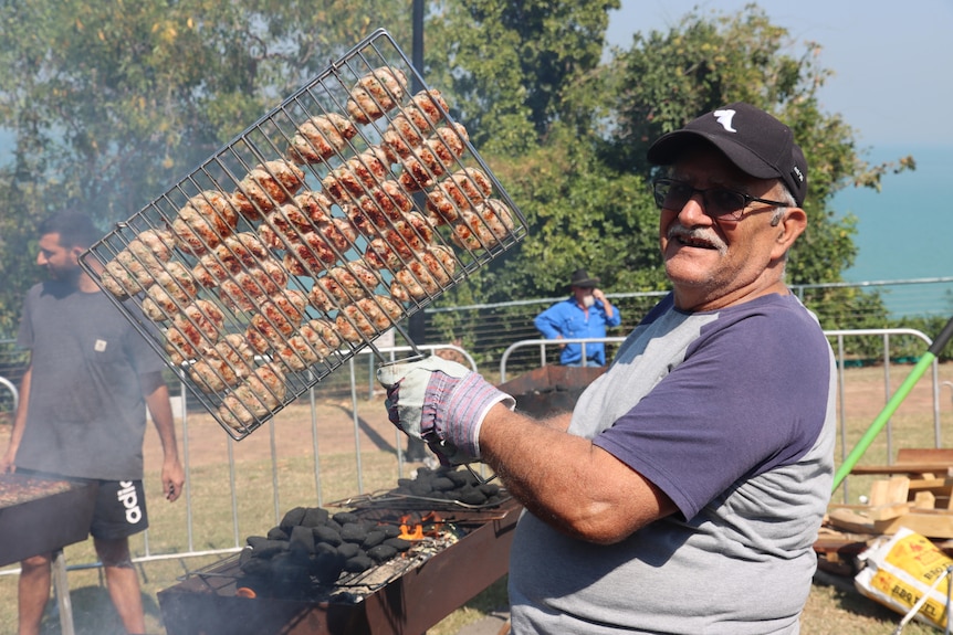 A happy man holds up some cooked meat and smiles for the camera.