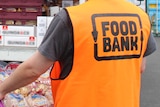 A Foodbank worker wearing an orange vest with insignia on back carrying a crate of Mighty Soft bread.