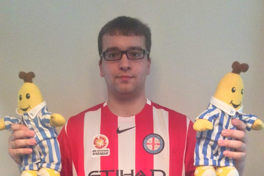 A man standing in front of a wall holds a Bananas in Pyjamas plush toy in each hand.