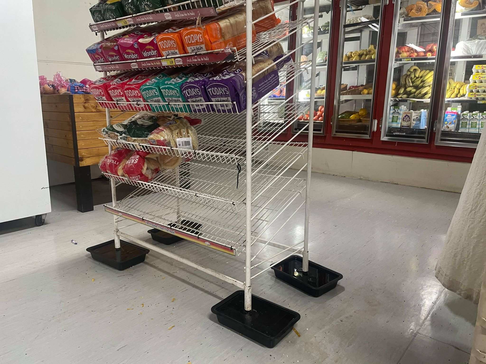 A shelf rack of loaves of bread on display has each leg in a bucket of water.