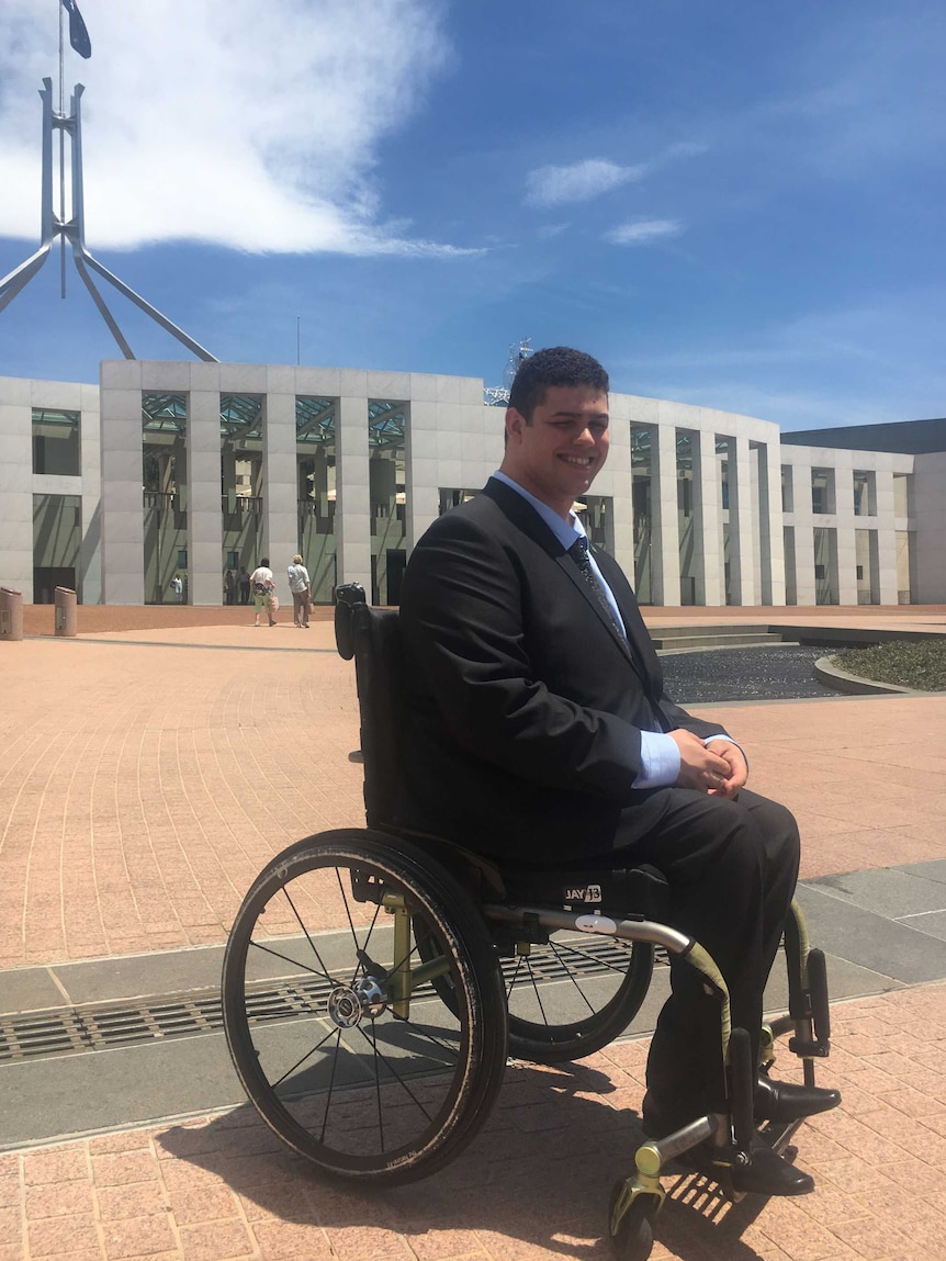 Jordon Steele-John smiles with his hands in his lap, sitting in his wheelchair out the front of Parliament House.