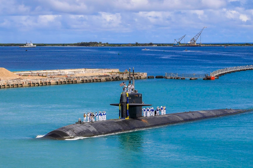 Naval personnel stand on top of a US Navy submarine sitting in a harbour