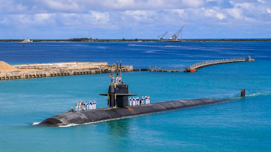 Naval personnel stand on top of a US Navy submarine sitting in a harbour