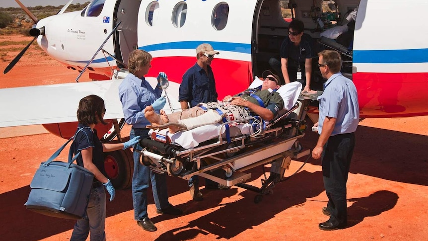 Man on stretcher in desert being loaded onto small aircraft.