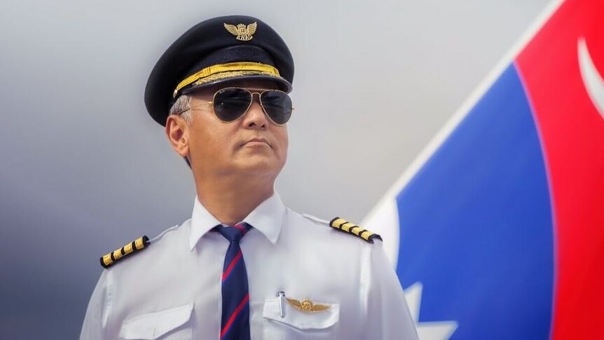 A pilot with sunglasses stands near a passenger plane.