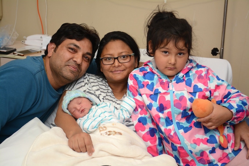 Mum, dad, baby and young daughter pose by a hospital bed.