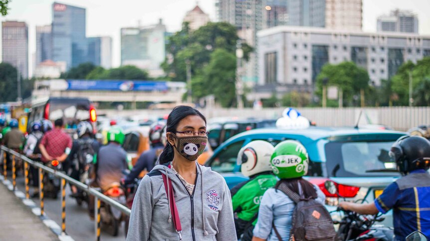 A woman walking down a street of Jakarta wearing mask