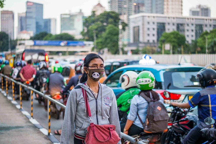 A woman walks down a Jakarta street wearing a mask