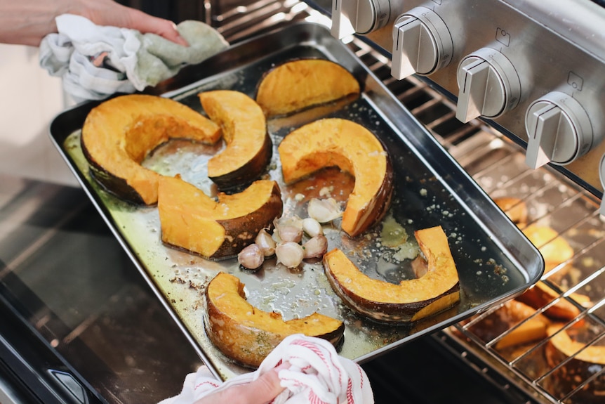 A person puts a tray in the oven, containing pumpkin slices and garlic cloves.