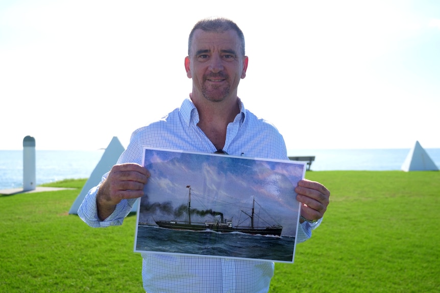 Hombre sujetando la foto de un viejo barco de vapor.