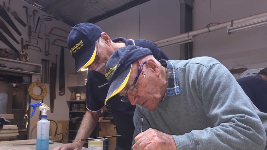 Two men leaning over a painting project in a workshop