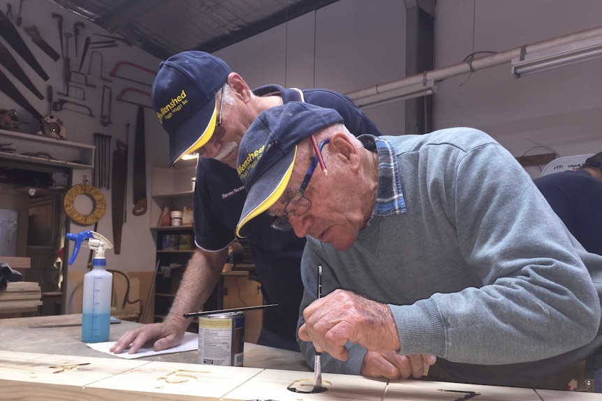 Two men leaning over a painting project in a workshop