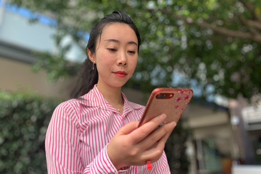 A woman looks at a smartphone she is holding.
