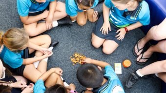 A group of students in blue shirts sit in a circle and play a game.