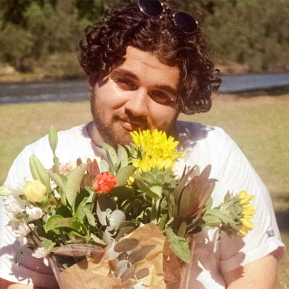 A man with curly hair and a beard holding a bunch of flowers