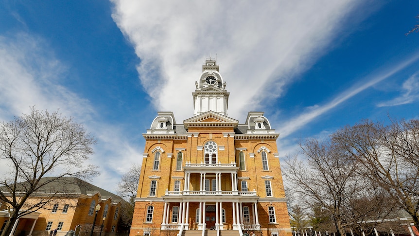 A low-angle photograph of Hillsdale College, a yellow-white building with a steeple.