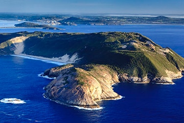 A sunlit granite headland in the foreground, with the bays, beaches and harbours of Albany in the background