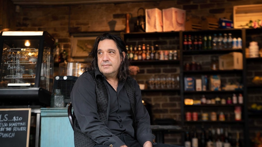 A man in black sits slouched on a chair in a bar