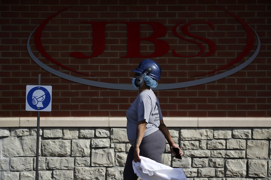 A worker wearing a protective mask walks past a logo reading JBS