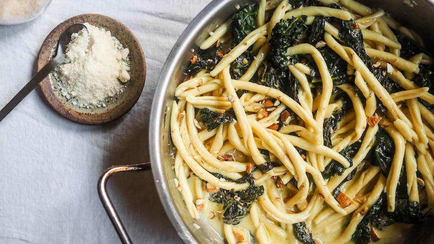 Two small dishes of sea salt and grated parmesan sit beside a pot of just cooked pasta with kale and almonds, a fast dinner.