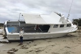 A boat on a beach with a woman standing in front of it.