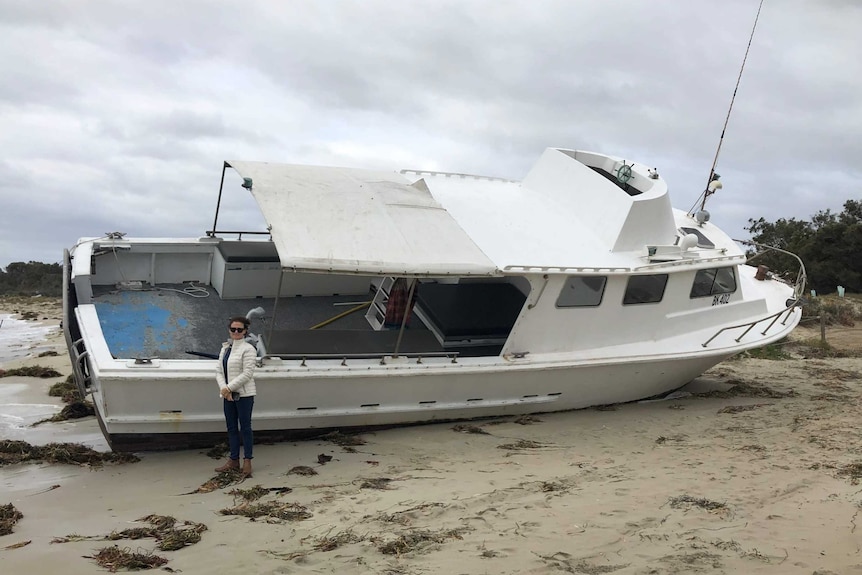 A boat on a beach with a woman standing in front of it.