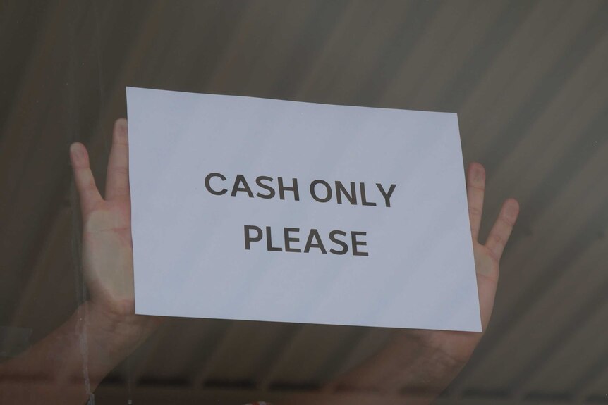A man puts 'cash only' sign on a shop window