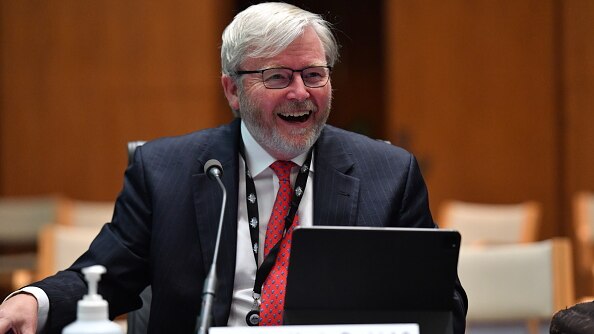 Former PM Kevin Rudd laughs while sitting at a desk