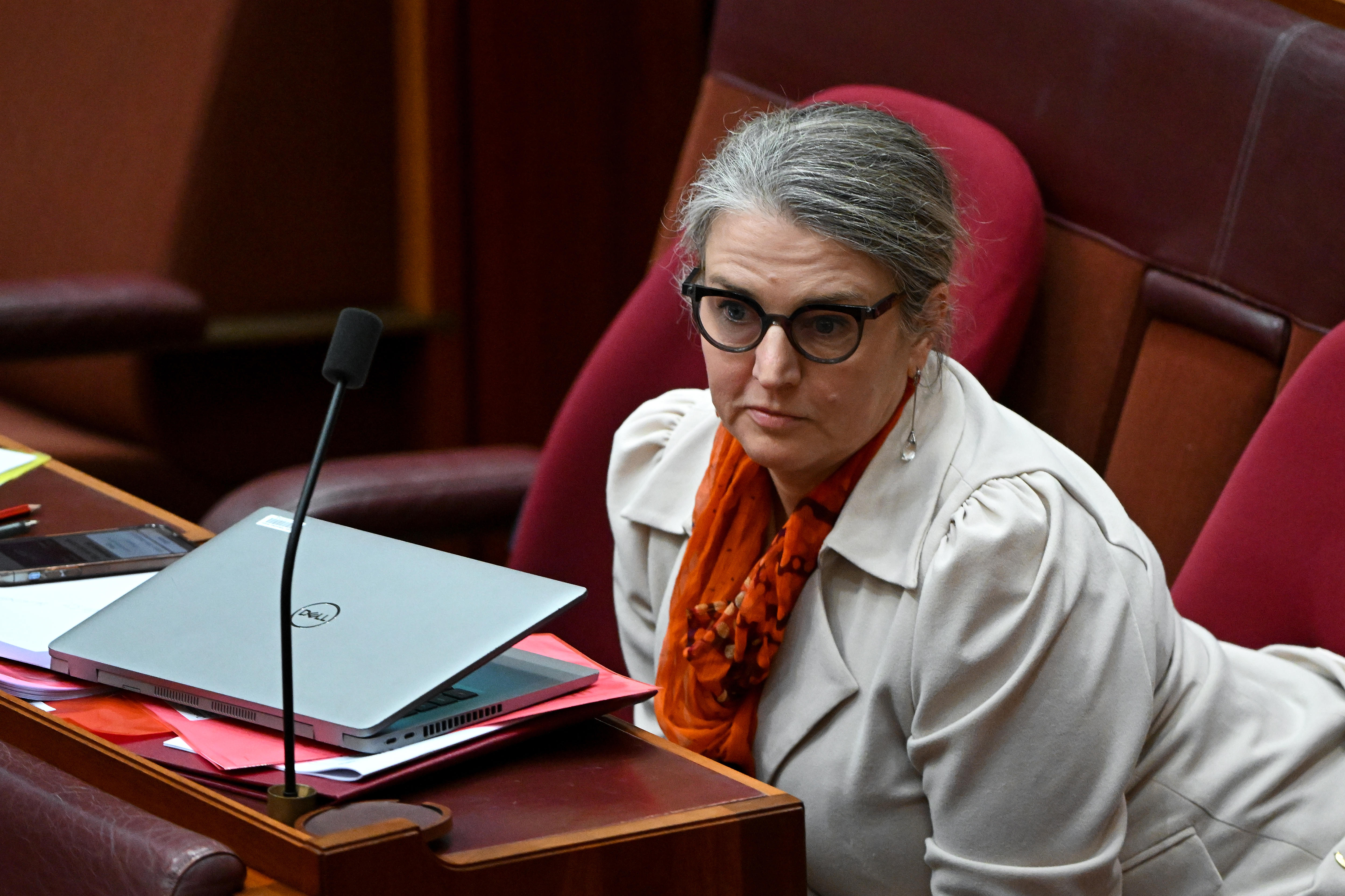 A woman wearing a cream-coloured jacket and a scarf sits on a red chair.