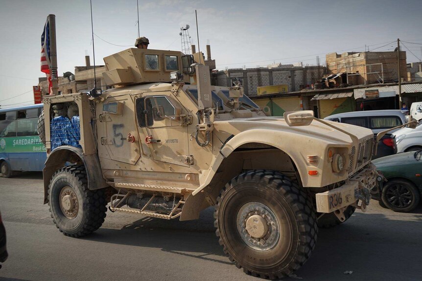 American military trucks with US flags flying drive among other traffic.