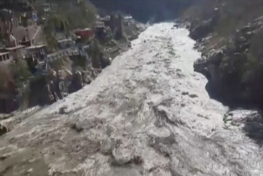 White and brown water of flooded river surges through a valley.