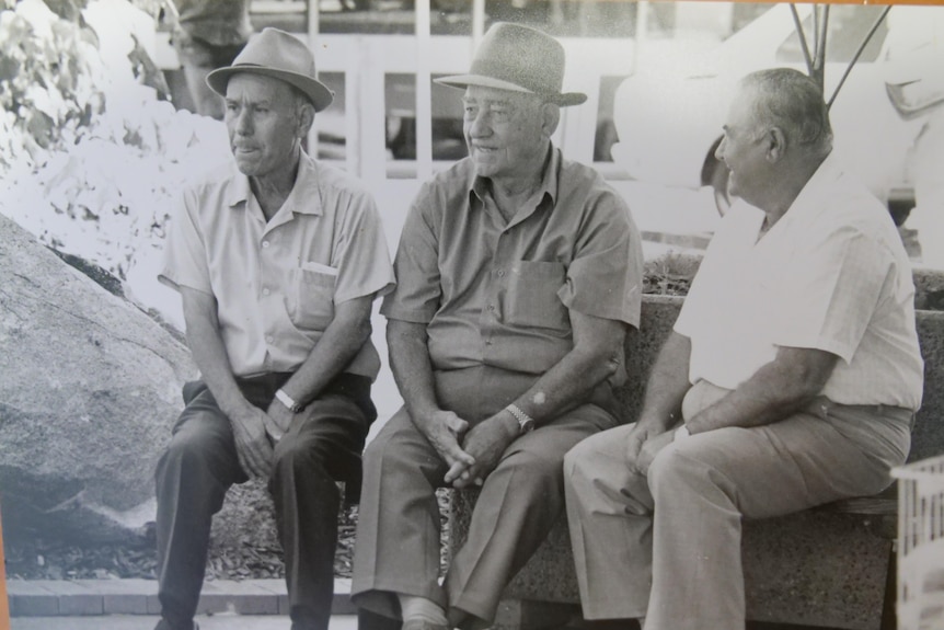 A black and white photograph of three men sitting on a bench