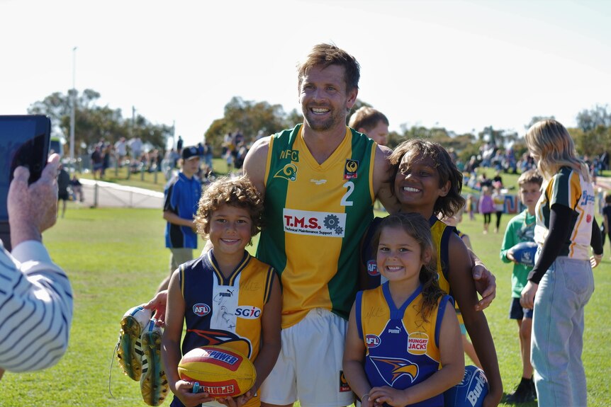 Мужчина в зелено-золотой футбольной форме с тремя детьми в футболке Eagles улыбается на фото  
