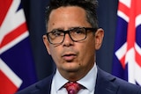 A head and shoulders shot of WA Treasurer Ben Wyatt standing in front of flags during a media conference.