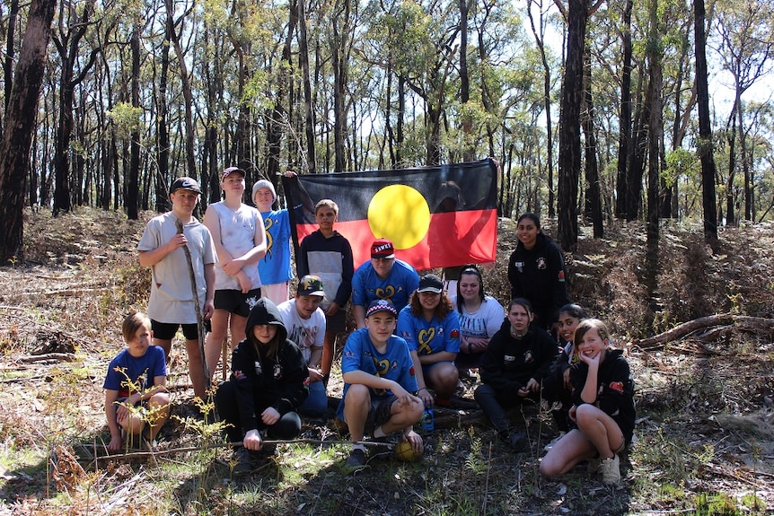 A group of Indigenous kids in a forest with an Aboriginal flag.